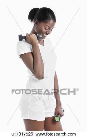 Stock Photograph - Thoughtful African American young woman with dumbbells standing over white background. Fotosearch