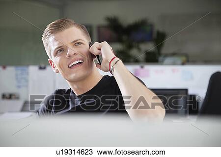 Thoughtful young man looking away while using cell phone at office View Large Photo Image Stock Image - Thoughtful young man looking away while using cell phone at office. Fotosearch