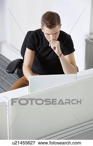 Thoughtful young man working at desk in office View Large Photo Image Stock Photo - Thoughtful young man working at desk in office. Fotosearch