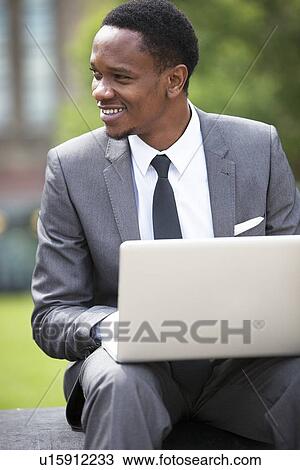 Three-quarter portrait of African American Businessman working on a laptop outdoors View Large Photo Image Stock Image - Three-quarter portrait of African American Businessman working on a laptop outdoors. Fotosearch