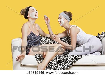 Two happy young women applying face pack while sitting on sofa over yellow background View Large Photo Image Stock Photograph - Two happy young women applying face pack while sitting on sofa over yellow background. Fotosearch