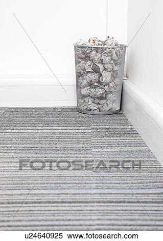 Stock Photography - Wastebasket full of crumpled paper in corner on carpet floor in room. Fotosearch