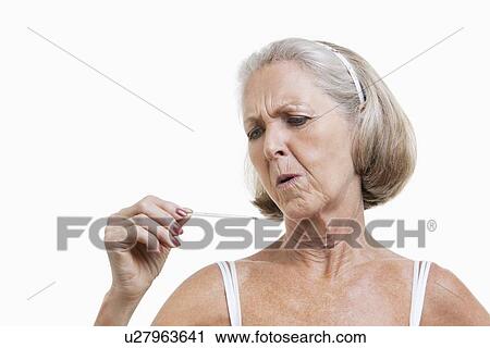 Stock Image - Worried senior woman checking thermometer against white background. Fotosearch
