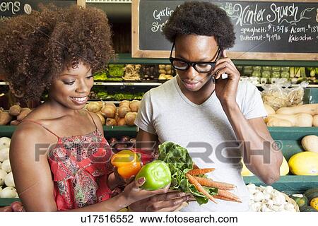 Stock Image - Young African American couple buying vegetables at supermarket. Fotosearch