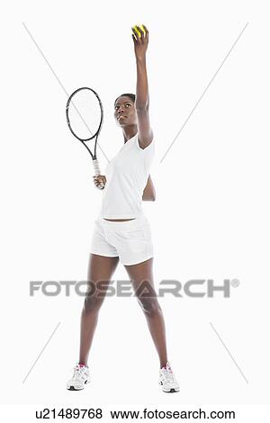 Stock Photo - Young African American woman serving tennis ball against white background. Fotosearch