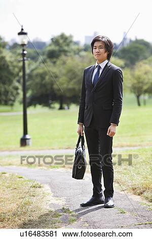 Young businessman carrying briefcase standing at park View Large Photo Image Stock Image - Young businessman carrying briefcase standing at park. Fotosearch