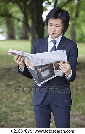 Stock Photography - Young businessman reading newspaper at park. Fotosearch