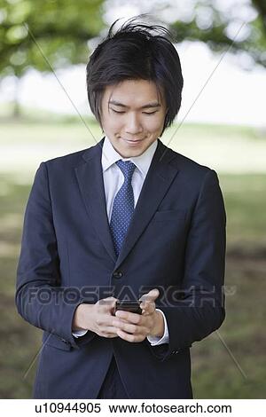 Stock Photography - Young businessman using cell phone at park. Fotosearch