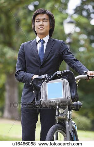 Young businessman with bicycle standing at park View Large Photo Image Stock Photo - Young businessman with bicycle standing at park. Fotosearch