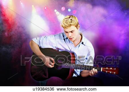 Stock Photograph - Young Caucasian man playing guitar in concert. Fotosearch