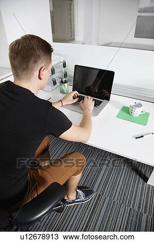 Stock Image - Young man working on laptop at office. Fotosearch