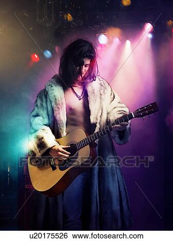 Stock Photograph - Young rock musician in fur coat playing guitar at concert. Fotosearch