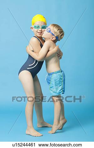 Young siblings in swimwear embracing and kissing over blue background View Large Photo Image Stock Image - Young siblings in swimwear embracing and kissing over blue background. Fotosearch