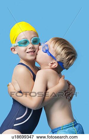 Young siblings in swimwear embracing and kissing over blue background View Large Photo Image Stock Photo - Young siblings in swimwear embracing and kissing over blue background. Fotosearch