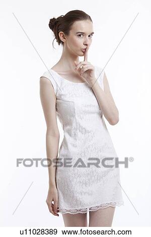 Young woman in dress gesturing to be quiet over white background View Large Photo Image Stock Photo - Young woman in dress gesturing to be quiet over white background. Fotosearch