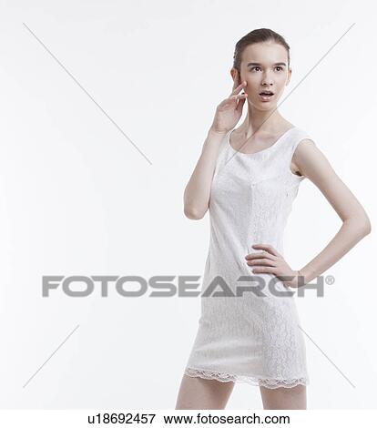 Stock Photo - Young woman in dress looking away with hand on hip over white background. Fotosearch