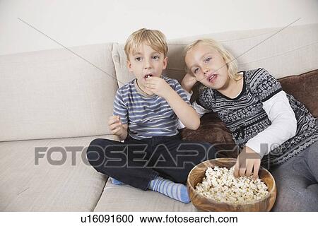 Brother and sister watching TV and eating popcorn View Large Photo Image Stock Image - Brother and sister watching TV and eating popcorn. Fotosearch