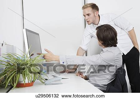 Stock Image - Businessman showing computer screen to coworker at desk. Fotosearch