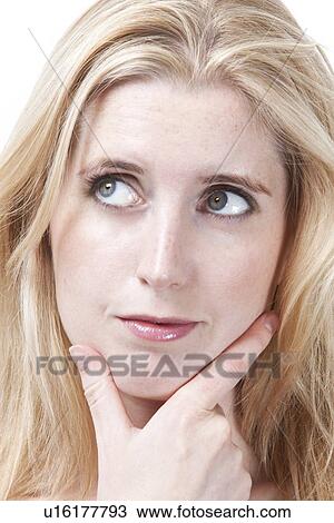 Stock Image - Close-up of thoughtful young woman with hand on chin looking away. Fotosearch