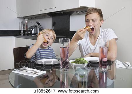 Stock Photo - Father and son eating pizza at breakfast table. Fotosearch