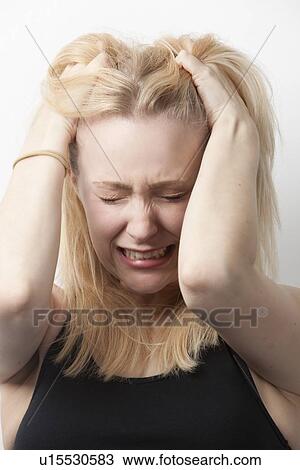 Stock Image - Frustrated young Caucasian woman with hands in hair against white background. Fotosearch