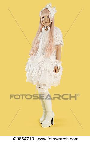 Stock Image - Full length portrait of young woman dressed as a doll over yellow background. Fotosearch
