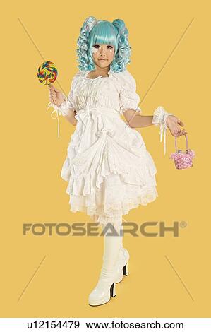 Full length portrait of young woman dressed as a doll holding lollipop over yellow background View Large Photo Image Stock Photo - Full length portrait of young woman dressed as a doll holding lollipop over yellow background. Fotosearch