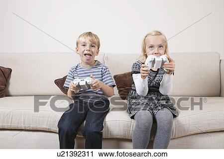 Stock Image - Happy brother and sister playing video game on sofa. Fotosearch