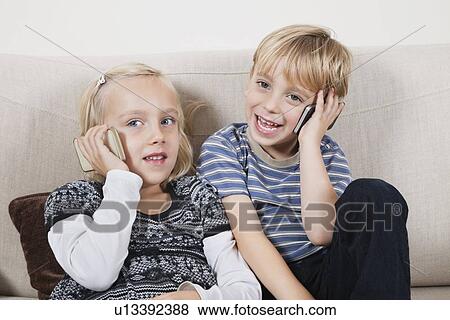 Happy brother and sister using cell phones at home View Large Photo Image Stock Photo - Happy brother and sister using cell phones at home. Fotosearch