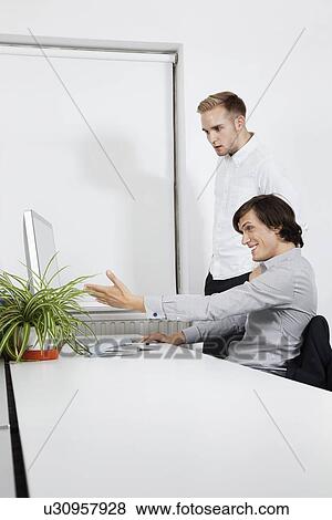 Happy businessman showing computer screen to coworker at desk View Large Photo Image Stock Photo - Happy businessman showing computer screen to coworker at desk. Fotosearch