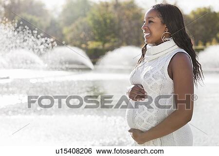 Stock Photograph - Happy young pregnant woman looking away in park. Fotosearch
