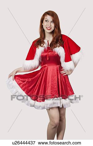 Stock Photo - Happy young woman in Santa costume standing against gray background. Fotosearch