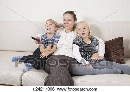 Stock Photograph - Happy young woman with children on sofa watching TV. Fotosearch
