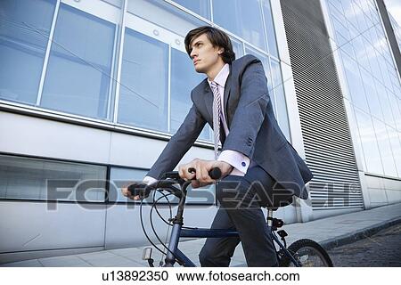 Low angle view of young businessman riding bicycle by building View Large Photo Image Stock Image - Low angle view of young businessman riding bicycle by building. Fotosearch