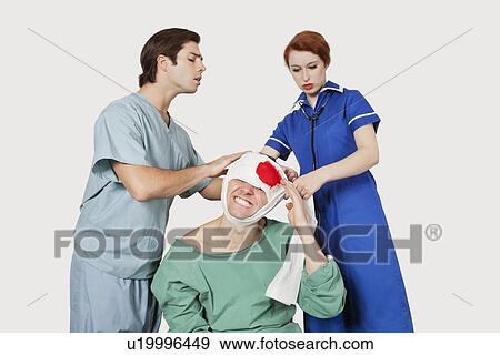 Stock Photo - Male doctor with female nurse bandaging an injured patient against gray background. Fotosearch
