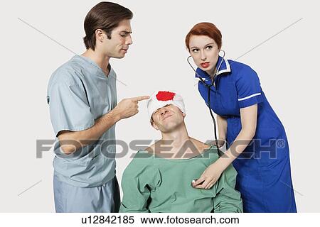 Stock Photography - Male doctor with female nurse examining an injured patient against gray background. Fotosearch