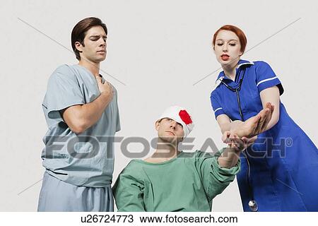 Stock Image - Male doctor with female nurse treating an injured patient against gray background. Fotosearch