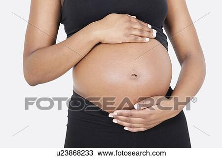 Stock Image - Mid section of pregnant woman touching abdomen over white background. Fotosearch