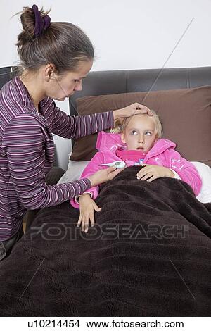 Mother checking unwell girl's temperature at home View Large Photo Image Picture - Mother checking unwell girl's temperature at home. Fotosearch