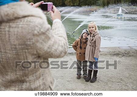 Stock Photo - Mother taking photo of children in front of fountain. Fotosearch