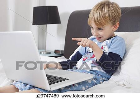 Playful Caucasian boy using laptop computer in bed View Large Photo Image Stock Photo - Playful Caucasian boy using laptop computer in bed. Fotosearch