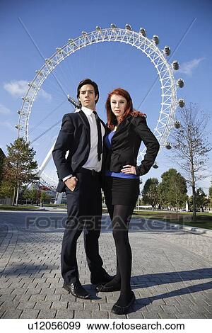 Stock Photo - Portrait of confident young business couple standing together against London Eye, London, UK. Fotosearch