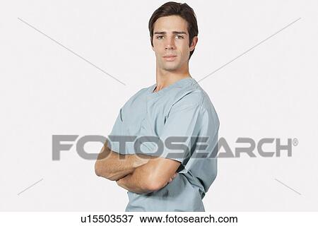 Stock Photo - Portrait of confident young man in surgical scrubs standing against gray background. Fotosearch
