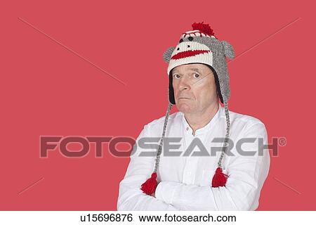 Stock Photograph - Portrait of confused senior man with arms crossed against red background. Fotosearch