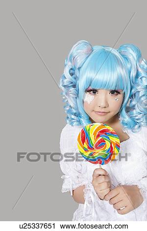 Portrait of cute young woman dressed as a doll holding lollipop over gray background View Large Photo Image Stock Image - Portrait of cute young woman dressed as a doll holding lollipop over gray background. Fotosearch
