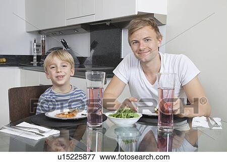 Stock Photo - Portrait of father and son smiling at breakfast table. Fotosearch