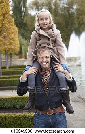Portrait of father carrying daughter on his shoulders at park View Large Photo Image Stock Photograph - Portrait of father carrying daughter on his shoulders at park. Fotosearch
