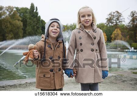 Portrait of happy brother and sister in trench coats holding hands at park View Large Photo Image Picture - Portrait of happy brother and sister in trench coats holding hands at park. Fotosearch