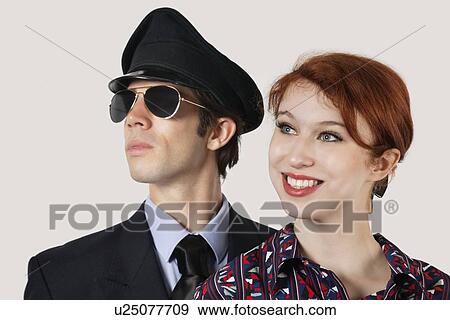 Stock Photo - Portrait of happy female flight attendant and pilot against gray background. Fotosearch