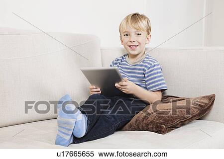 Portrait of happy young boy holding tablet PC on sofa View Large Photo Image Stock Photography - Portrait of happy young boy holding tablet PC on sofa. Fotosearch